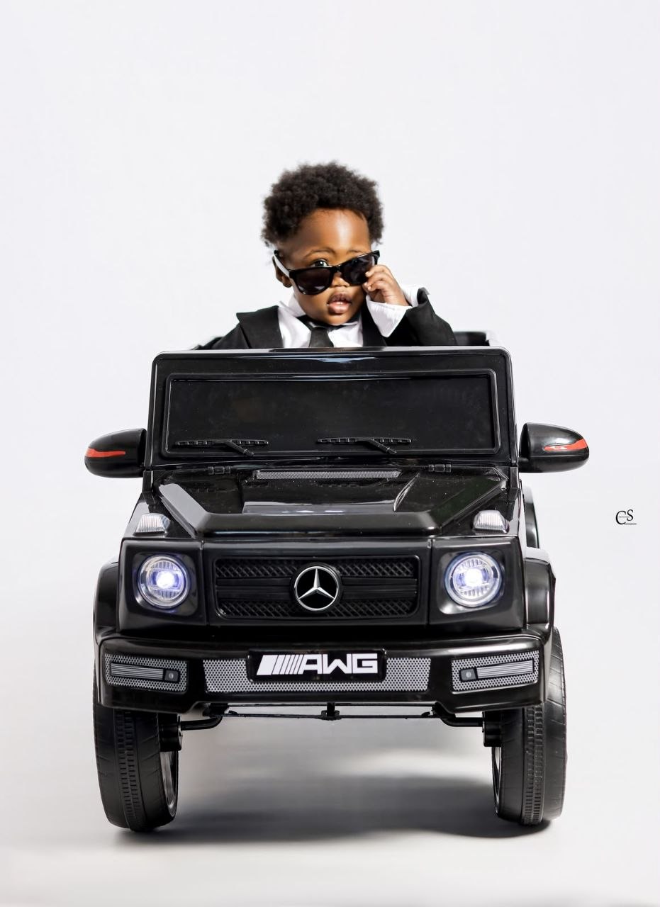 Baby boy wearing sunglasses in a black toy car