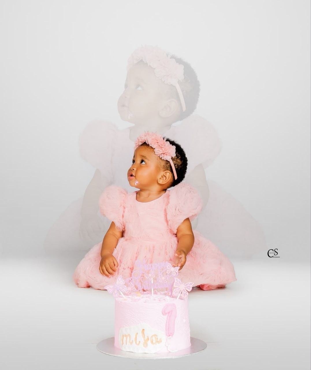 Baby girl posing with her pink first birthday cake