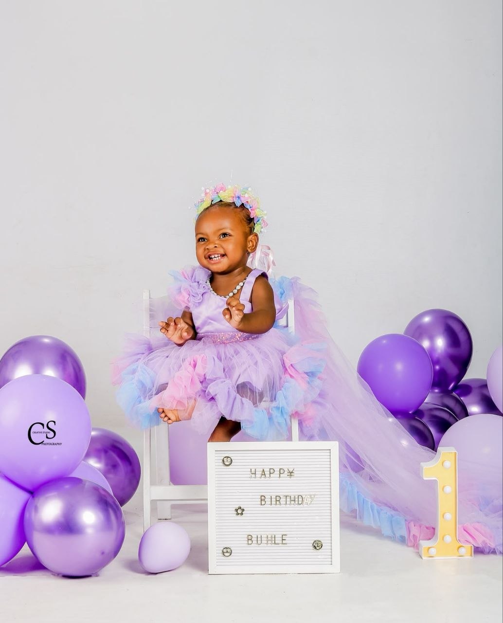 Baby girl surrounded by purple first birthday balloons